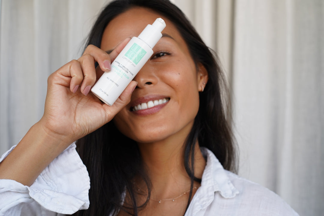 Woman holding a bottle of LUMION Skin Save My Skin Serum in front of her face. 